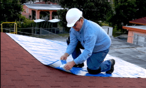 Man on roof lays out a tarp to temporarily stop a roof leak