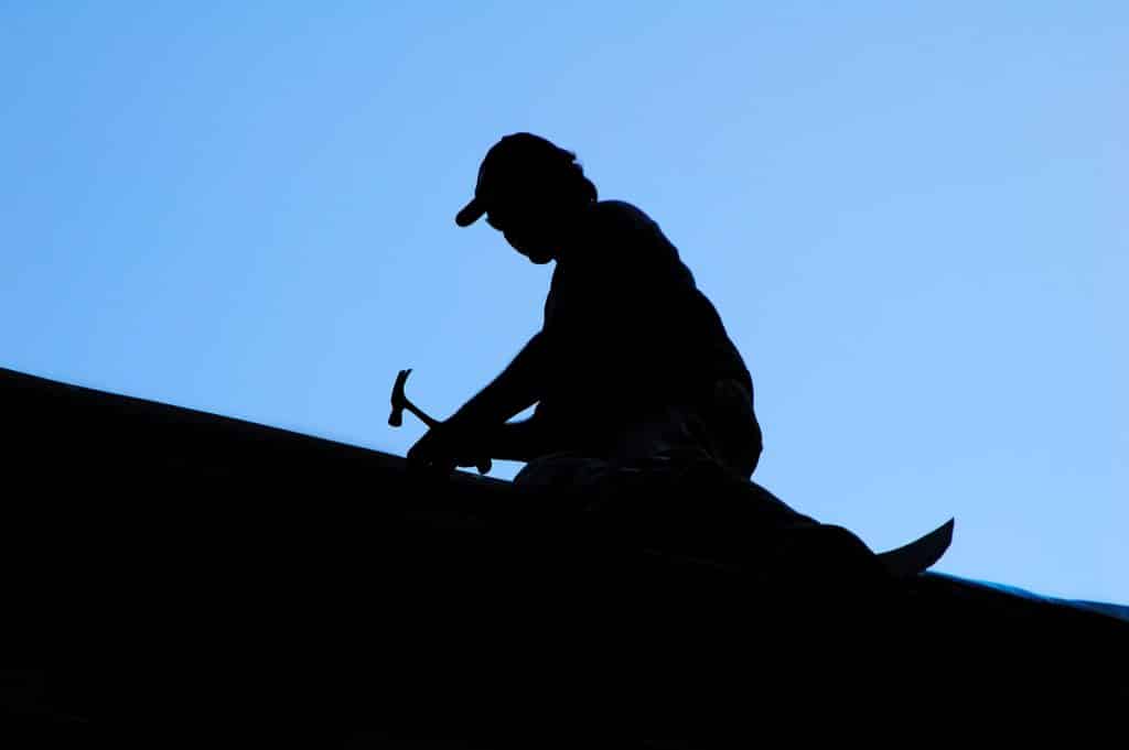 A silhouette of a man fixing the roof with a hammer
